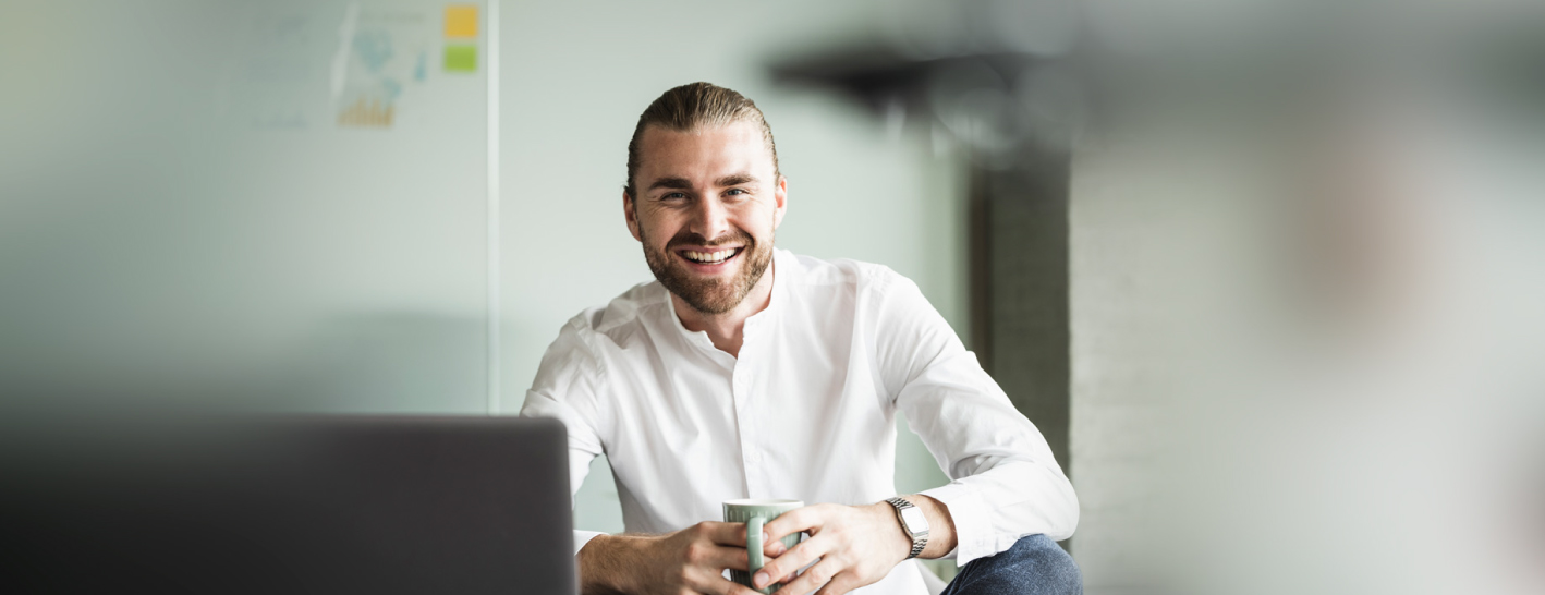 Chico feliz tomando café frente a una computadora