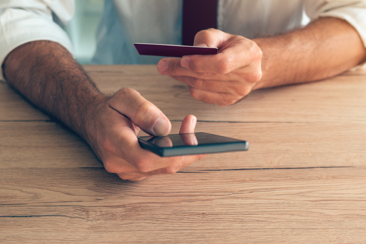 Consejos para proteger tu dinero de fraudes y estafas con tus tarjetas Protege tu dinero de fraudes y estafas con tarjetas - hombre con celular en la mano haciendo transacción con tarjeta