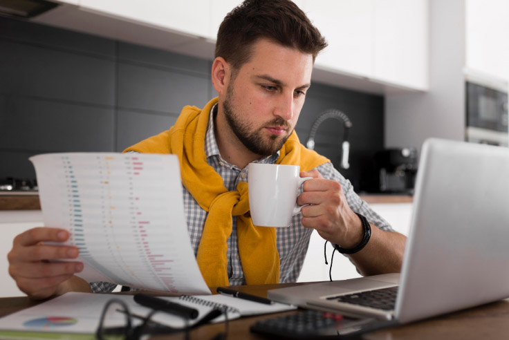 Aprende a gestionar tus deudas Hombre trabajando con documentos y laptop, con una taza de café en la mano