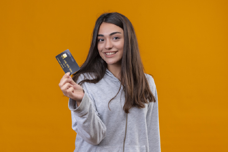 Tipos de tarjetas bancarias Mujer joven de cabello largo con sweater gris y tarjeta bancaria en la mano