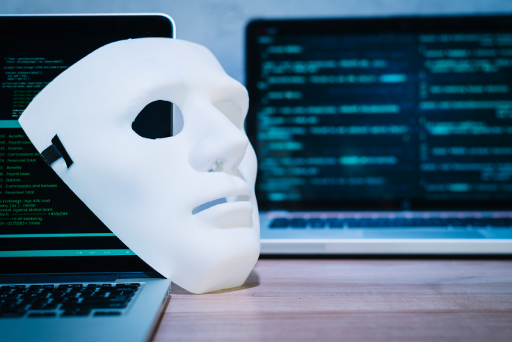 Protege tus contraseñas y datos del phishing Máscara de hacker blanca descansa sobre pantalla de una laptop que está en una mesa. Al fondo se distingue otra laptop