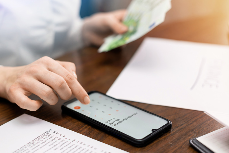 Mujer utilizando la calculadora de su celular mientras contabiliza billetes y organiza sus finanzas personales 