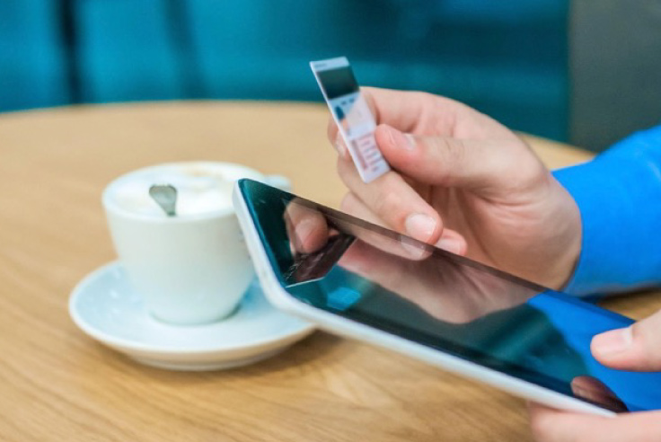 Primer plano de manos de hombre realizando una compra en línea con tablet y tarjeta de crédito, junto a una taza de café