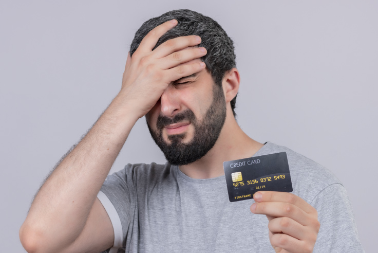 Hombre con mano en la cabeza, angustiado porque su historial crediticio se afectó por deuda y retrasos en pagar su tarjeta